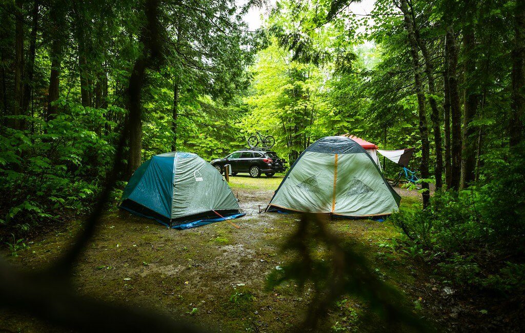 a campground with two tents and a vehicle with bicycle on top