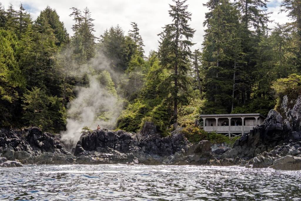 A person sitting on a rock as steam rises from a hot spring at Hot Springs Cove in Tofino (photo: Destination BC/Ben Girardi)